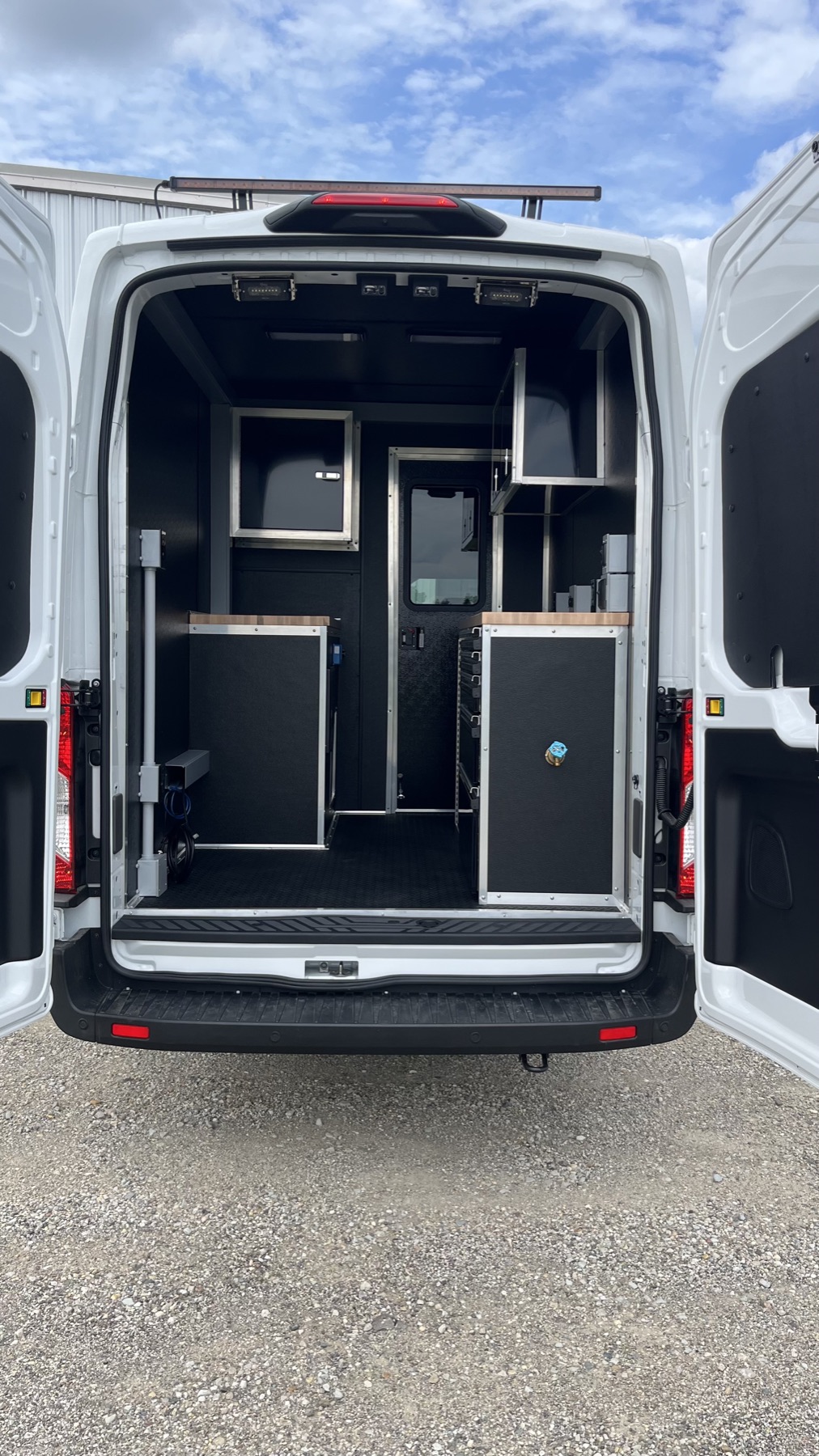 Blacked-out cargo van interior with custom aluminum cabinetry, wood countertops, and integrated LED lighting