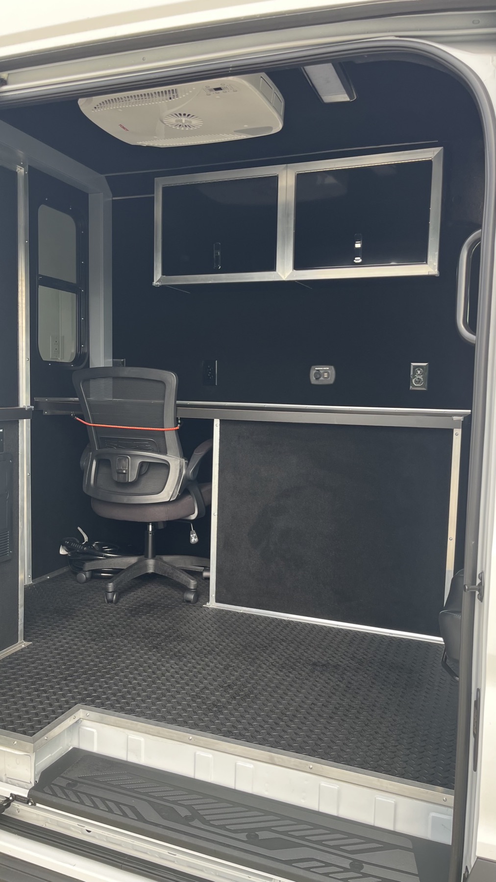 Mobile office build inside a cargo van with an office chair and overhead cabinets