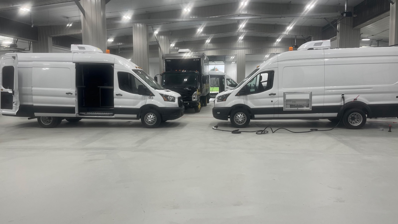 Two completed white cargo vans parked inside the V Tech Conversions shop, ready for delivery